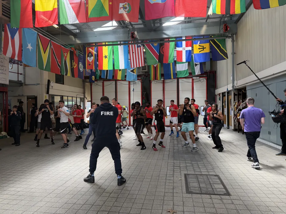 A firefighter leads boxers and firefighters through a shadowboxing drill beneath international flags at North Kensington Fire Station