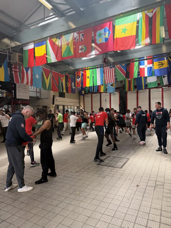 A coach helps a boxer with his gloves while the hall trains behind them