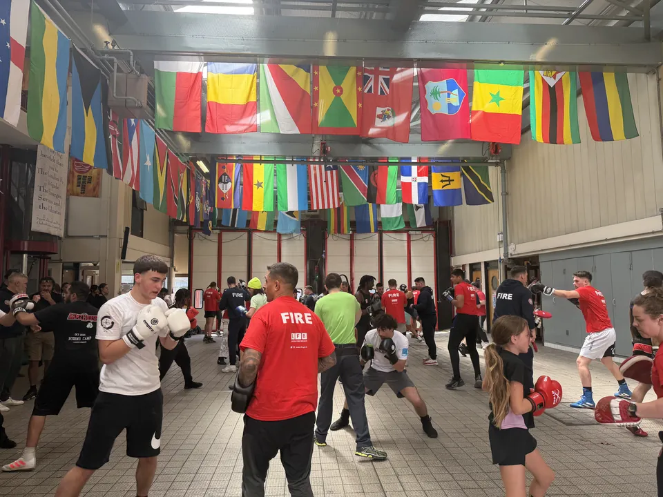 A boxer keeps his guard up beside a firefighter holding pads, with a young boxer training nearby