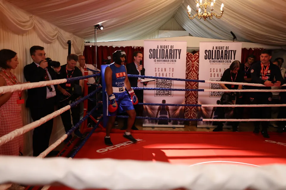 A boxer waits in the ring as photographers and camera crews gather ringside