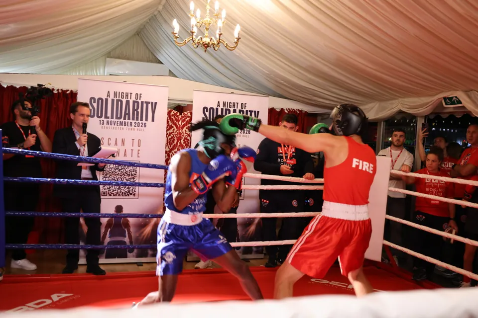 A boxer in a red FIRE vest throws a long jab at an opponent in blue