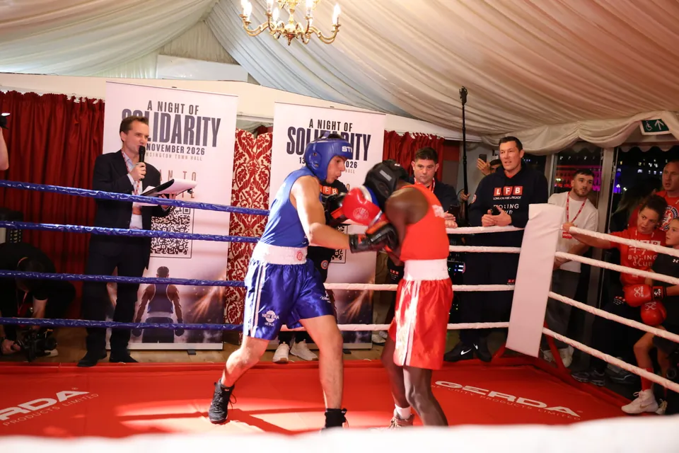 A close exchange between boxers in blue and red as coaches watch from ringside