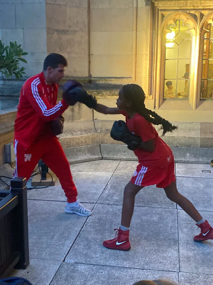 A young boxer lands a jab on a coach's pad beside a Gothic window on the terrace