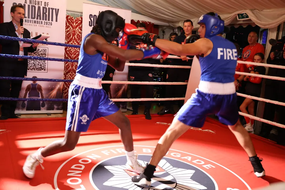 A boxer lands a jab across the London Fire Brigade Boxing Club crest on the ring canvas