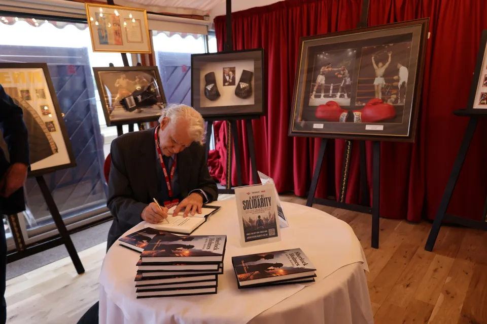A guest signs books beside framed boxing memorabilia